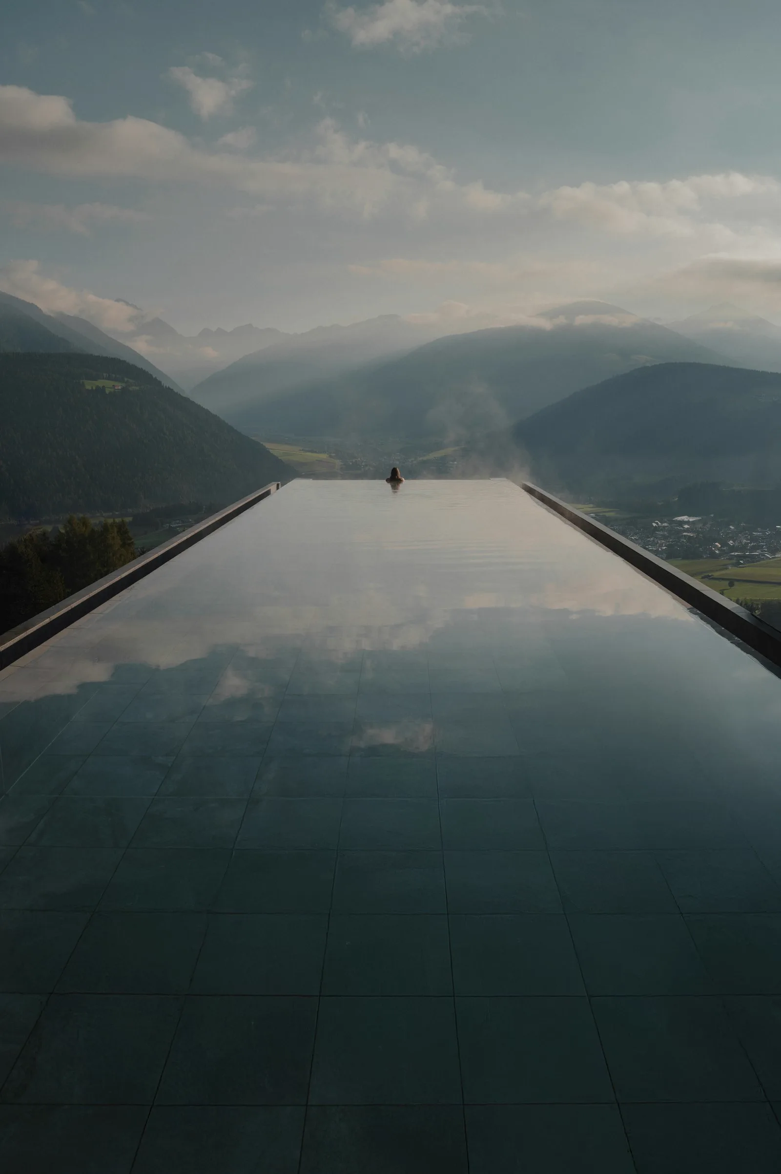 Guest relaxing in an infinity pool overlooking misty mountains