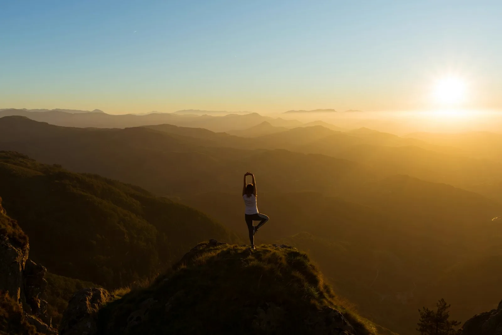 Guest doing a yoga pose on a mountain summit at sunrise